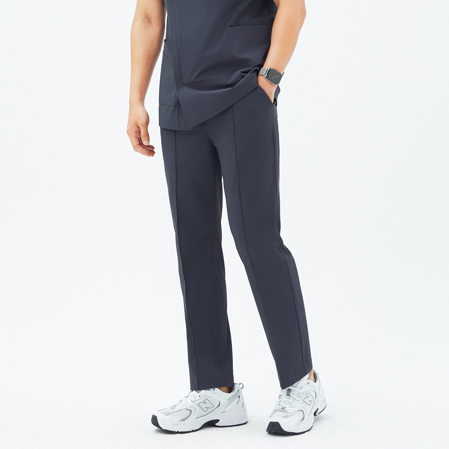 Image of Close-up of a male model wearing TUL Men’s Premium Banding Pants in Deep Gray, showing the front seams, straight-leg cut, and hands in pockets. The scrub top matches the pants, and the model’s watch is visible on his left wrist.